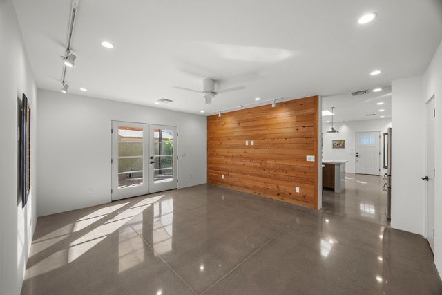 Empty modern living room with French doors, wood accent wall, and polished concrete floor.