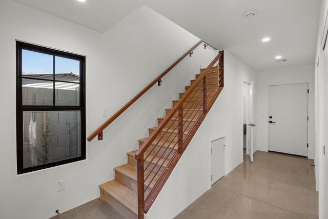 Staircase with wooden steps and railing, leading to an upper level. Black-framed window and white walls.
