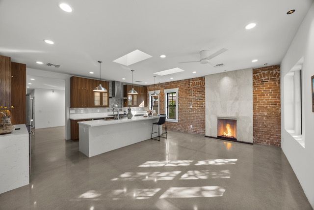 Spacious modern kitchen with a large island, brick wall fireplace, and concrete floors.