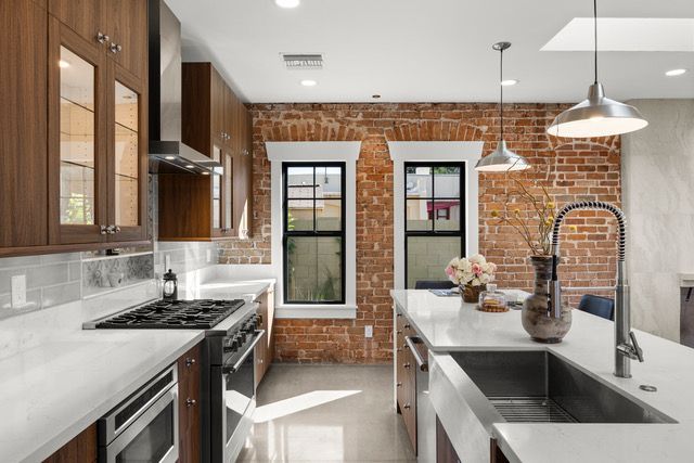 Modern kitchen with exposed brick wall, white countertops, and stainless steel appliances.
