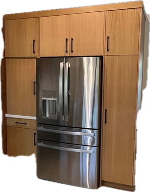 Stainless steel refrigerator surrounded by light wood cabinets with black handles.