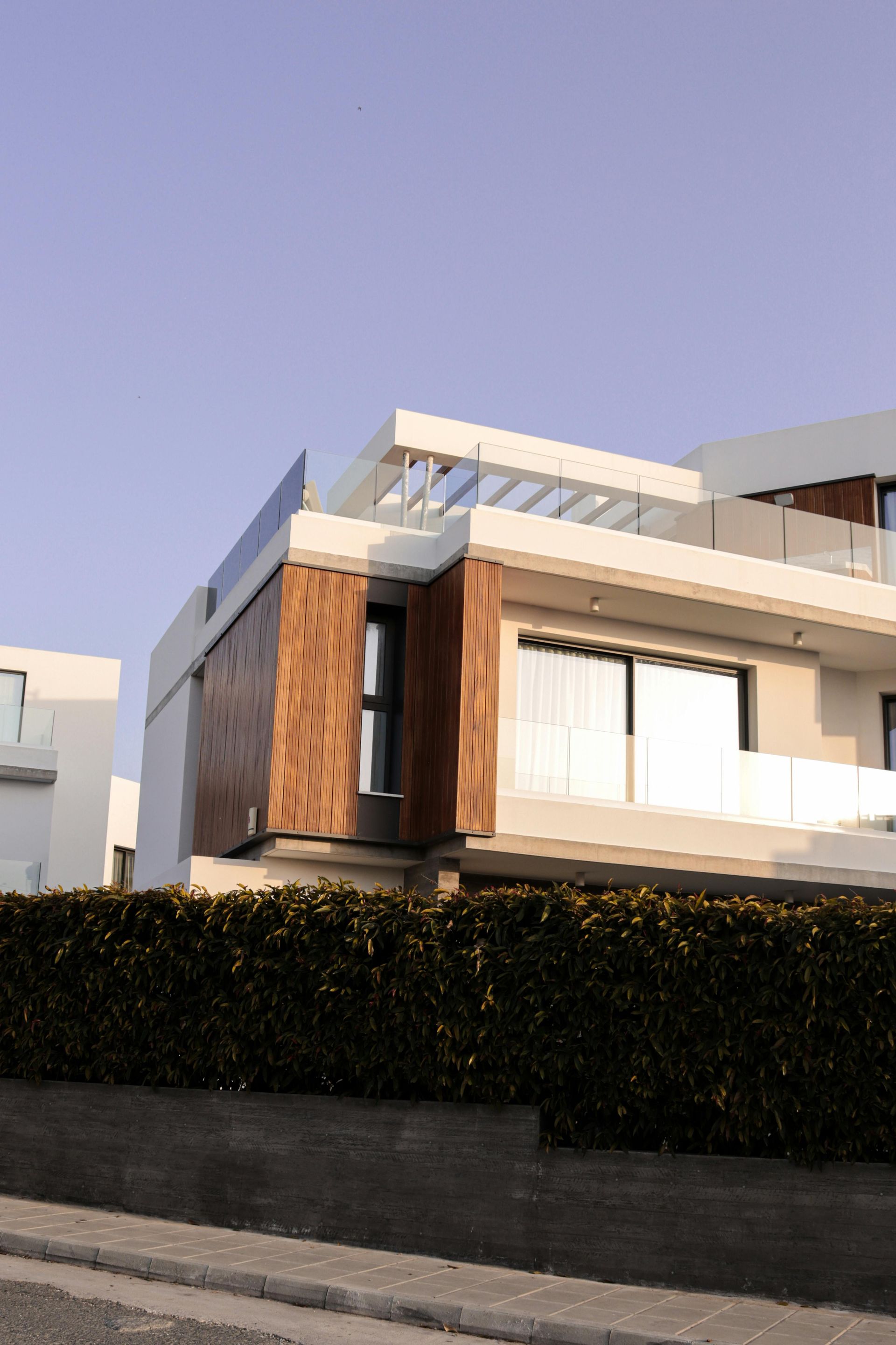 Modern two-story house with wooden paneling, a glass railing, and a hedge in front of it.