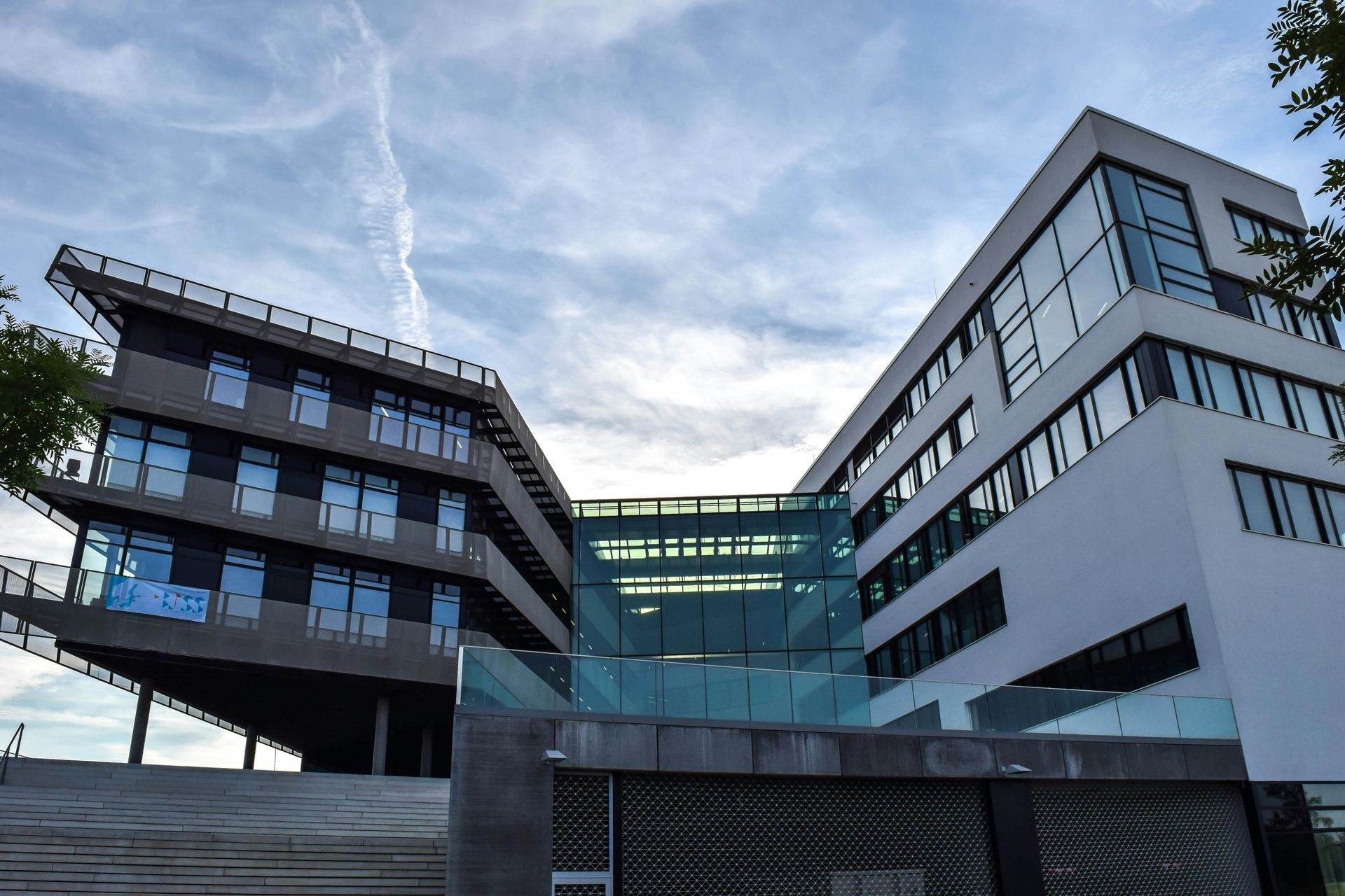 Modern office building with glass and white facades, against a cloudy sky.