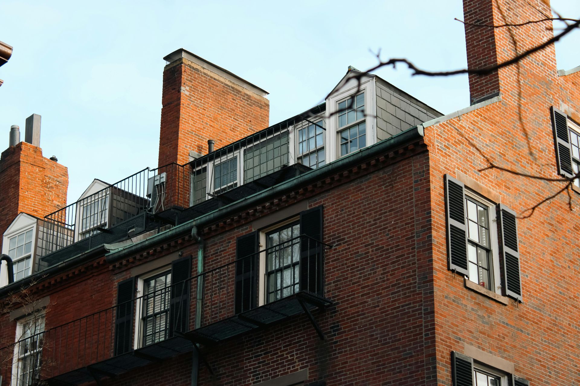 Brick buildings with chimneys, windows, and black shutters, against a blue sky.