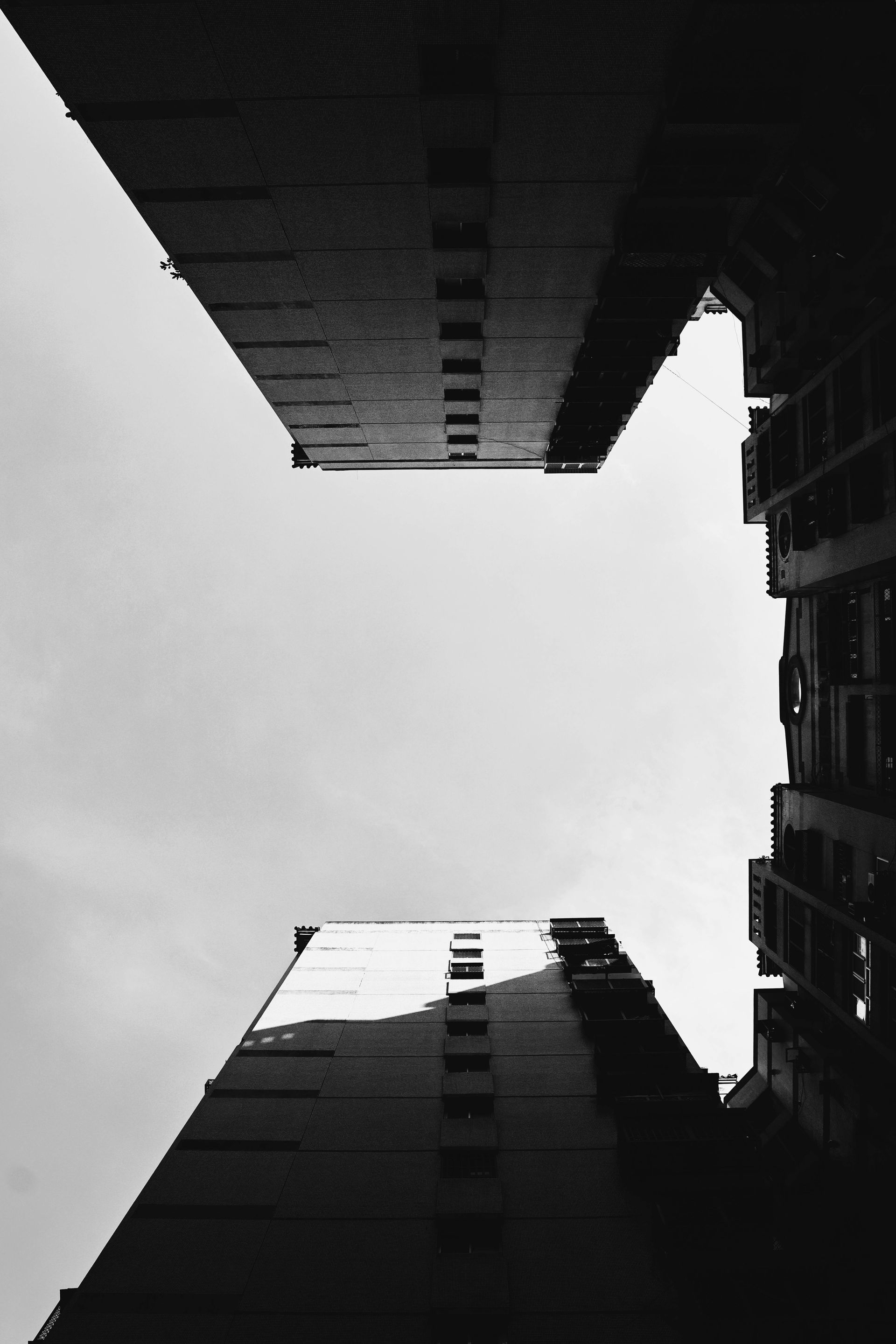 Black and white shot looking up at two tall buildings framing a view of the sky.