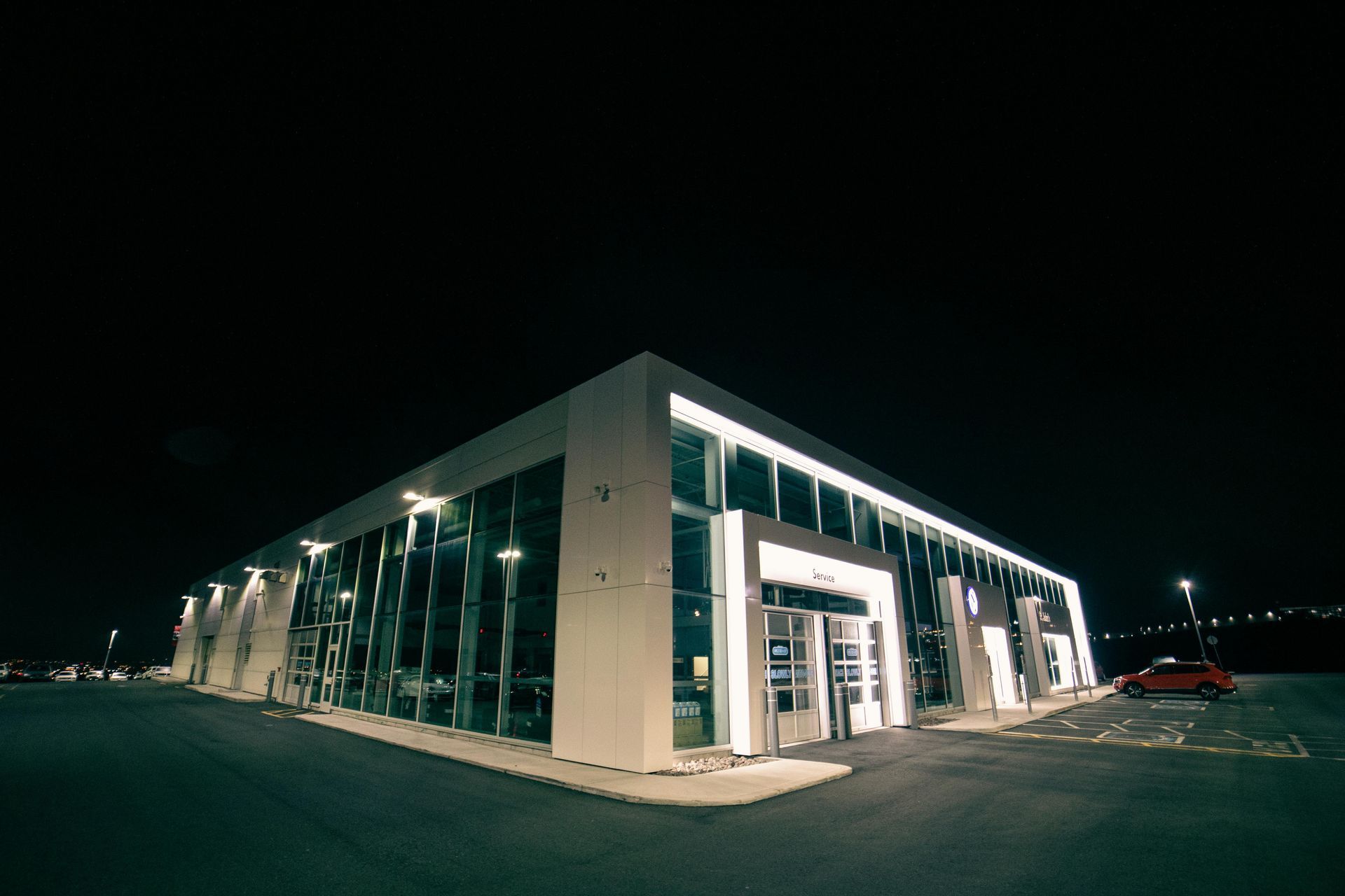 Illuminated modern building at night with glass windows and a car parked in front.