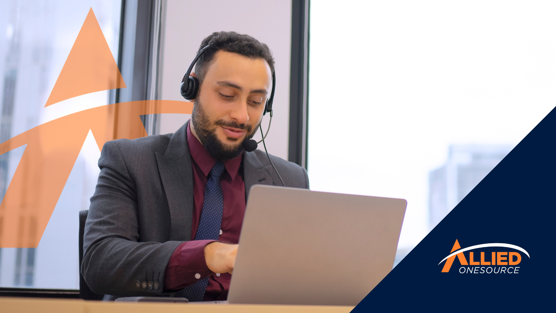 A professional in a headset and suit prepares for a call center interview using his laptop.