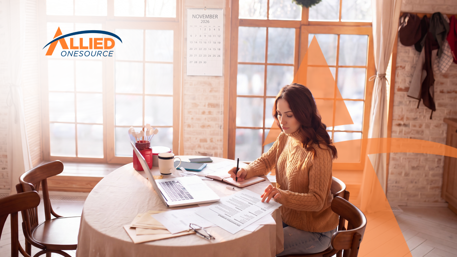 A woman works at a round table by sunny windows, taking notes beside a laptop and a printed resume.