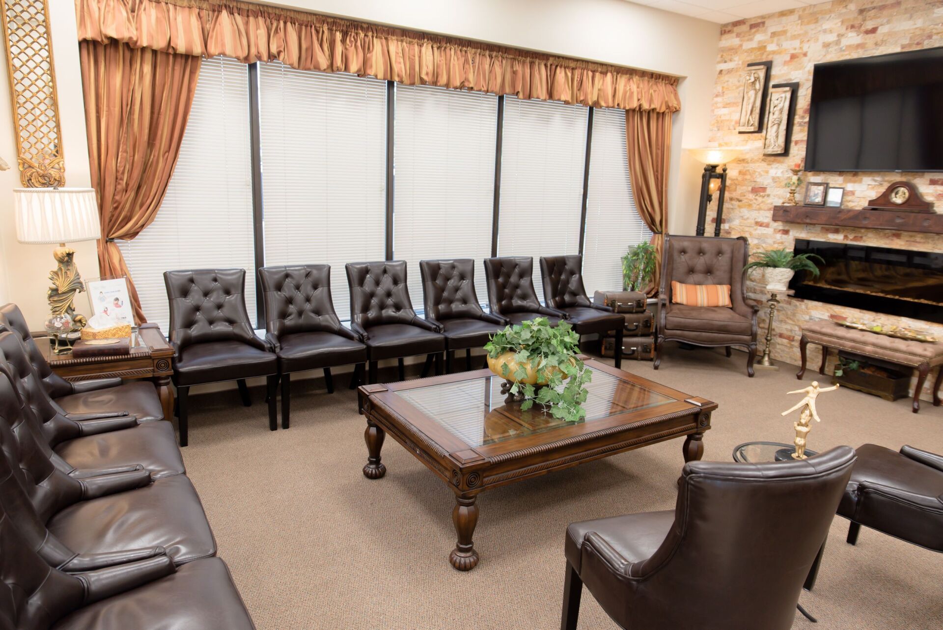 A waiting room with a couch , chairs , coffee table and television.