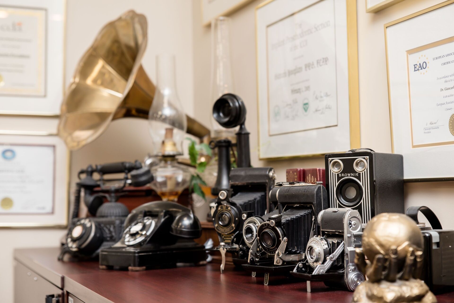 A collection of old phones , cameras , and a phonograph on a table.