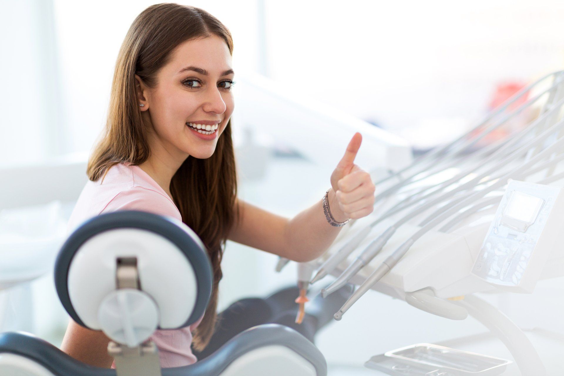 A woman is sitting in a dental chair and giving a thumbs up.