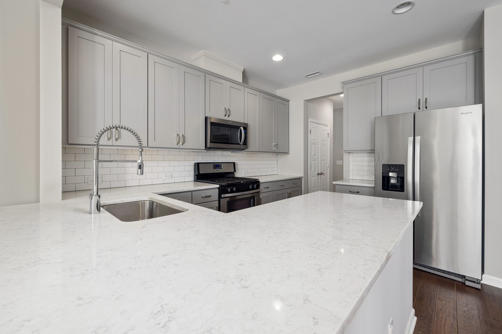 Bright modern kitchen with white cabinets, island, stainless appliances, and wood floors
