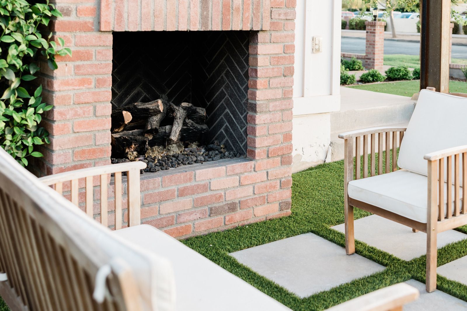 Patio with brick fireplace, white chairs, and grass pavers in a modern outdoor seating area