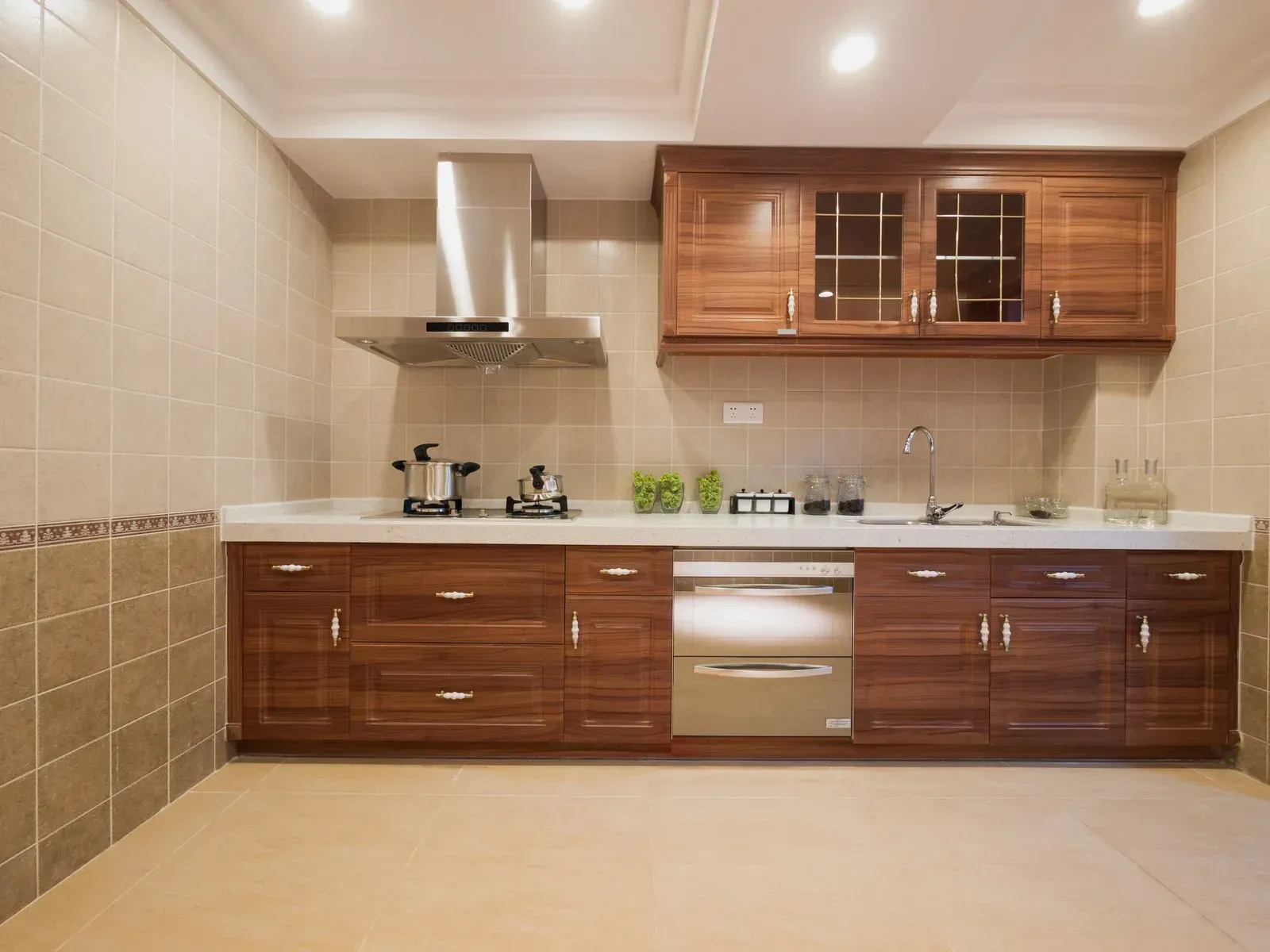 Modern kitchen with beige tile walls, wood cabinets, stainless steel appliances, and a light tile floor