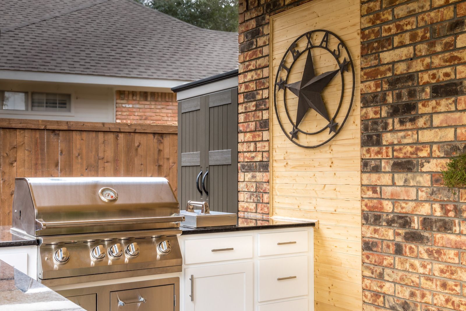 Outdoor patio kitchen with stainless grill, white cabinets, and a star wall decoration on a brick wall