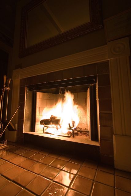 Lit fireplace in a dim room with glossy tiled hearth and mantelpiece