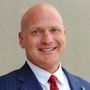 A bald man in a suit and tie is smiling for the camera.