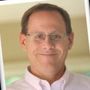 A man wearing glasses and a white shirt is smiling for the camera.