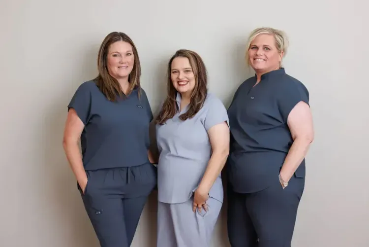 Three people standing against a light wall, wearing matching navy and light blue outfits.