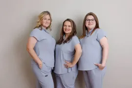 Three people in matching light gray outfits pose against a neutral studio background.