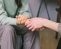Two people holding hands in a comforting gesture indoors