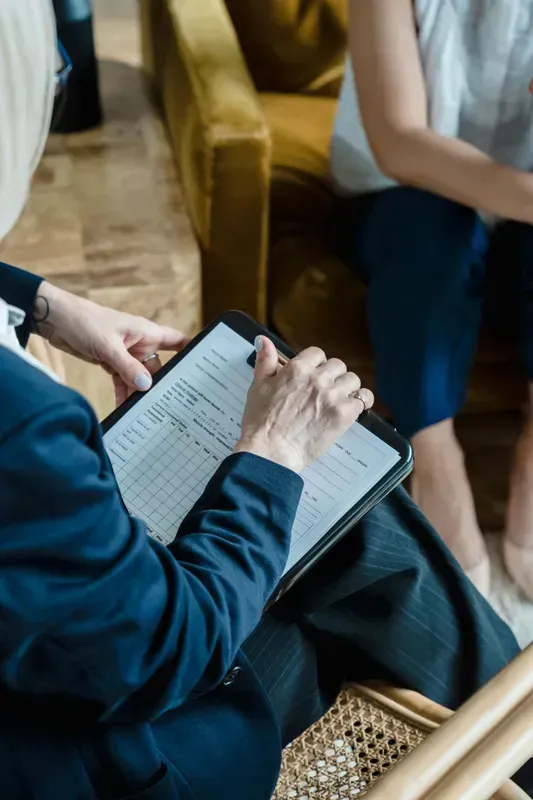 Person taking notes on a tablet in a meeting room, seated beside a woven tray and a wooden chair