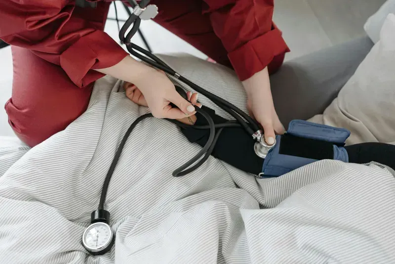 Person taking a blood pressure reading on a person in bed with a cuff and stethoscope