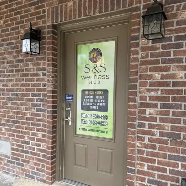 Brick storefront entrance for S&S Wellness Spa with tan door and posted hours sign