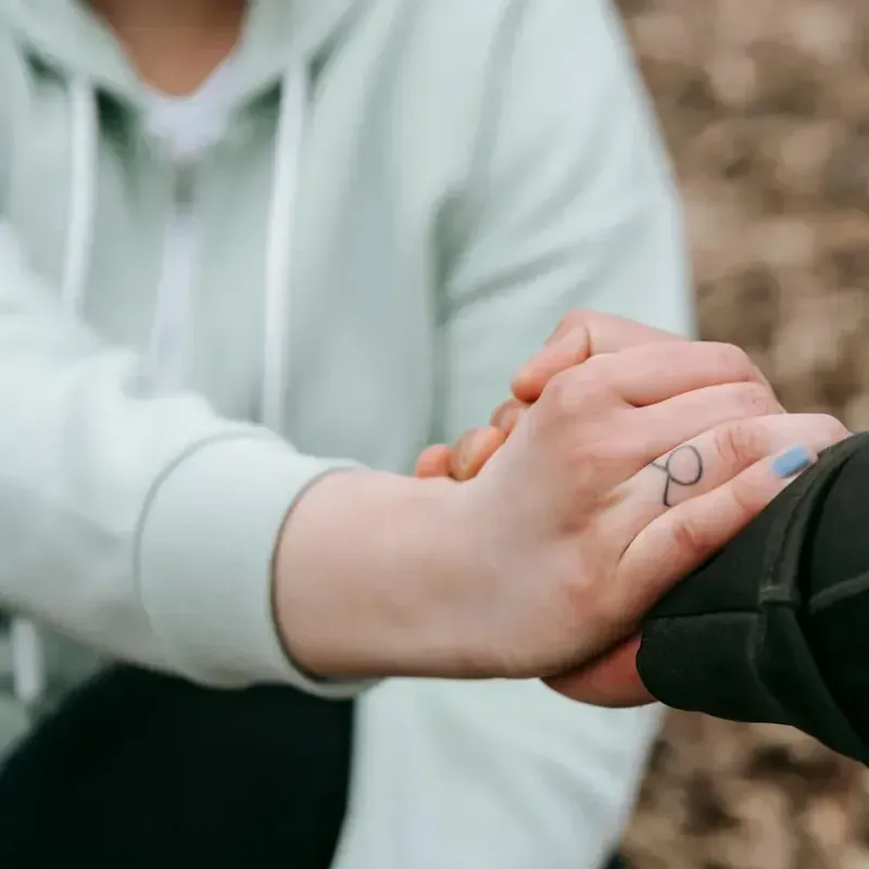Two people holding hands in a close-up, one wearing a light mint hoodie and the other a black sleeve.