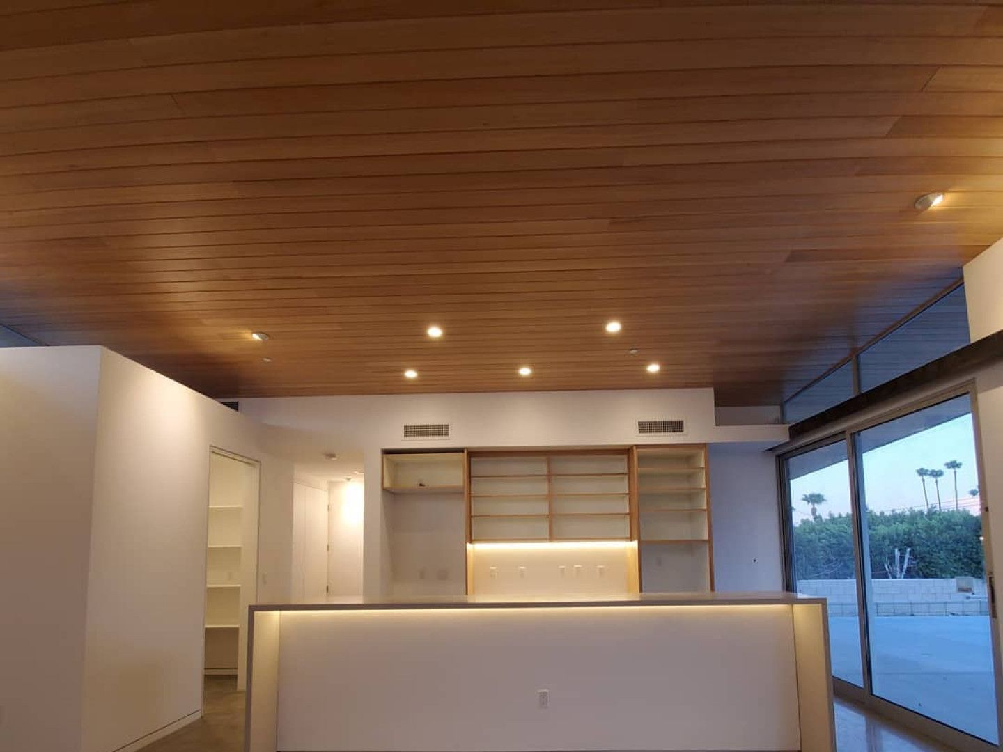 Modern minimalist kitchen with warm wood ceiling, white cabinetry, and large window view
