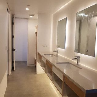 Modern restroom with long double sink counter, large mirrors, and beige tile floor in a bright hallway