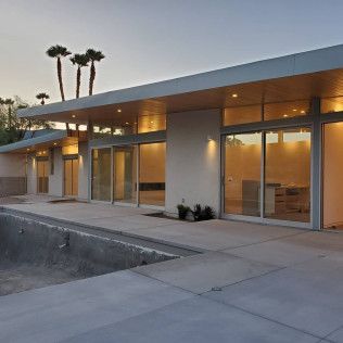 Modern low-rise building with glass windows, warm interior lights, and a concrete walkway at dusk