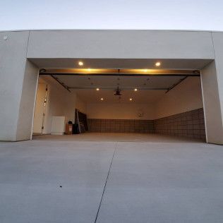 Empty two-car garage with open door, beige walls, and ceiling lights at dusk