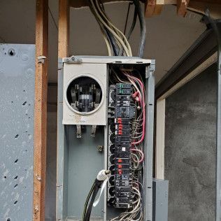 Open electrical breaker panel with exposed wiring and circuits in a utility area