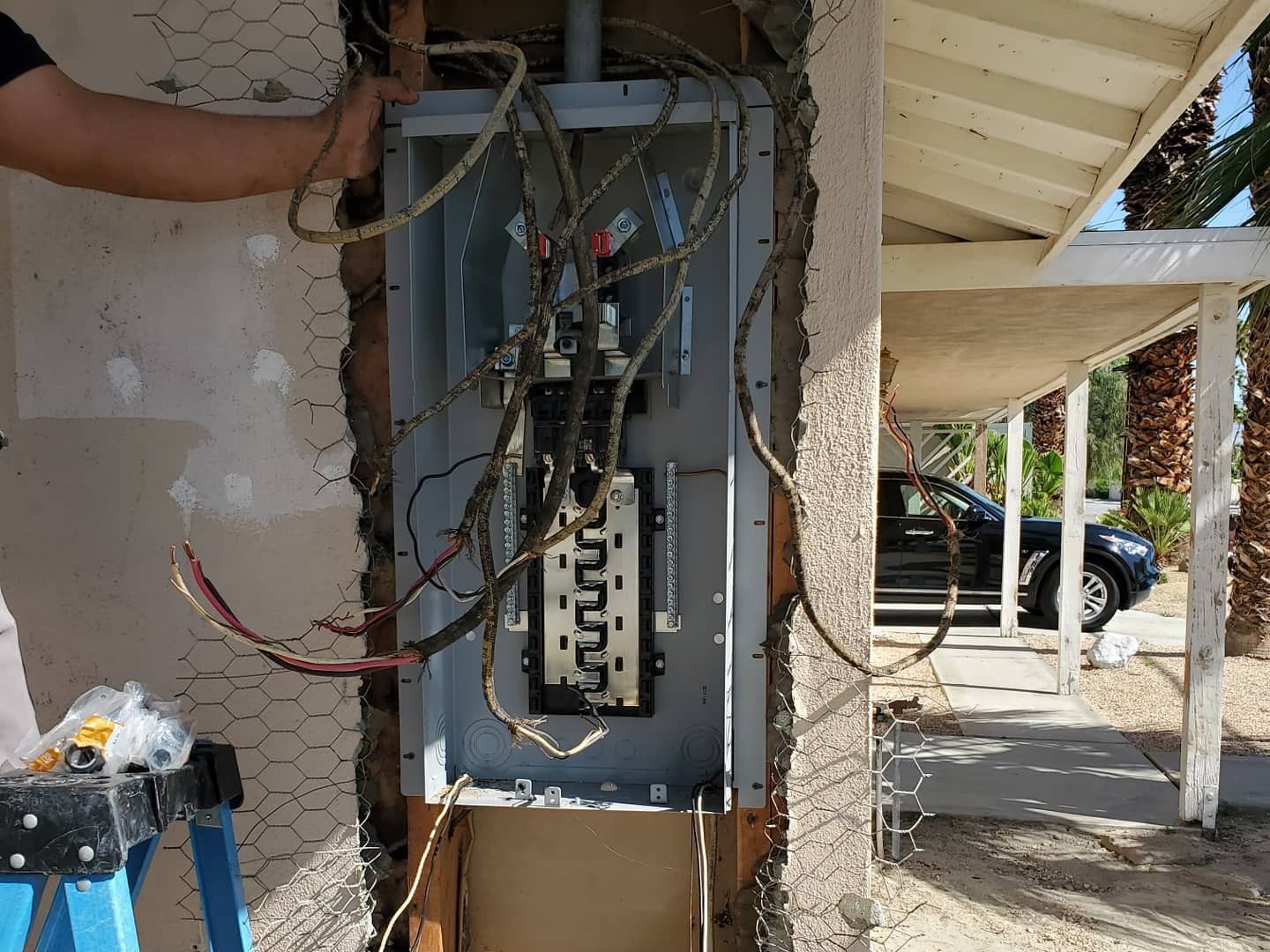 Open electrical panel with exposed wiring mounted on an exterior wall under a porch