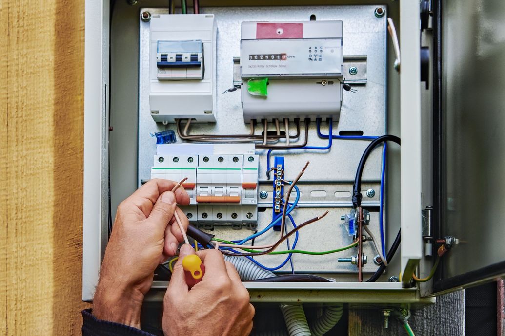 Hands wiring an open electrical panel with circuit breakers and blue cables