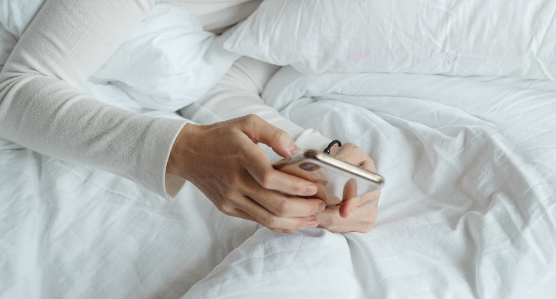 Een persoon ligt in bed en gebruikt een mobiele telefoon.