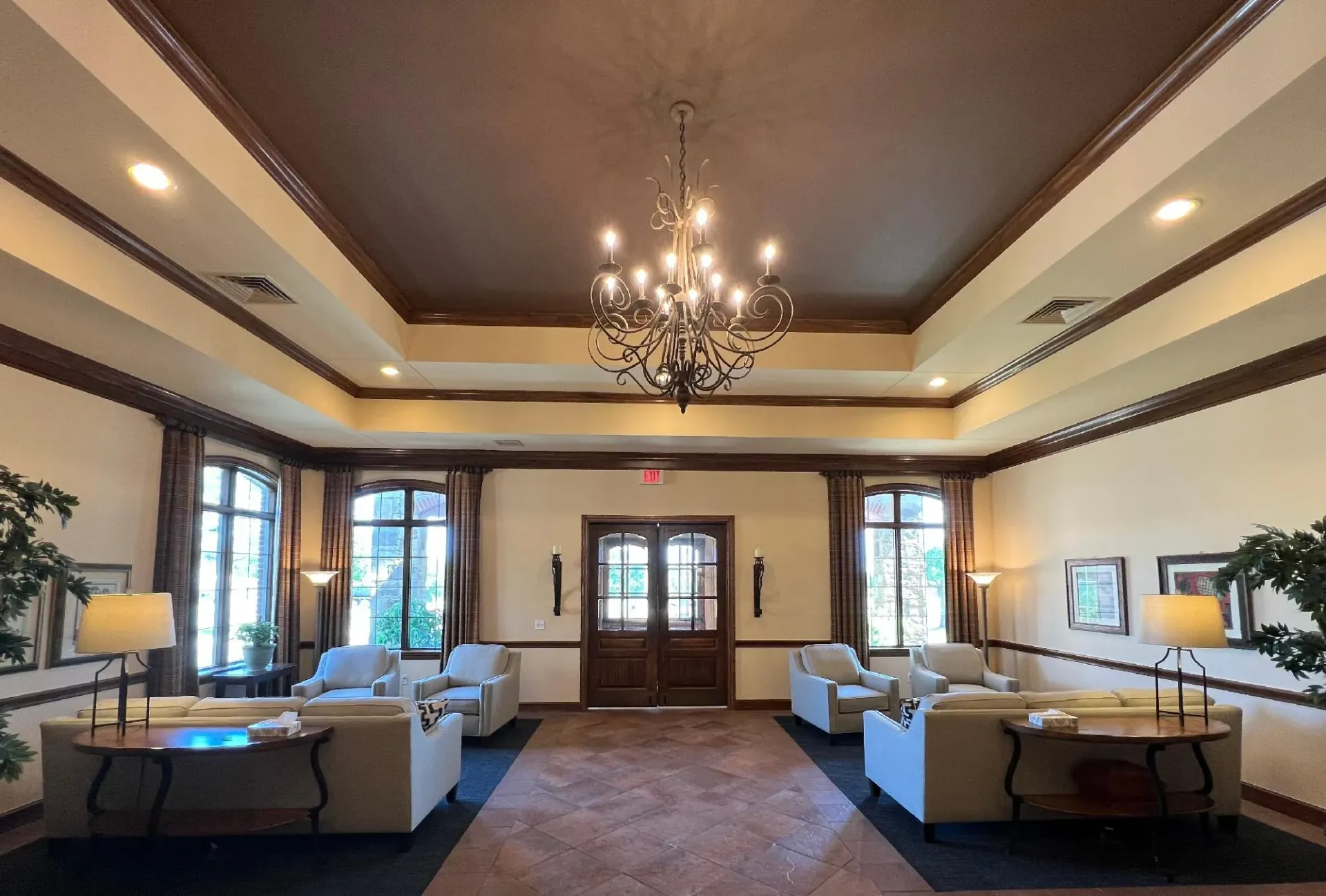 Elegant lobby with chandelier, beige sofas, and tall windows under a coffered ceiling