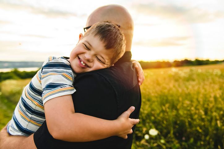 Child smiling while hugging an adult in a sunlit field at sunset