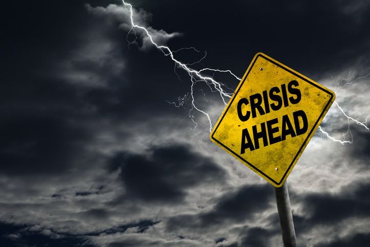Yellow “CRISIS AHEAD” warning sign against dark storm clouds with lightning.
