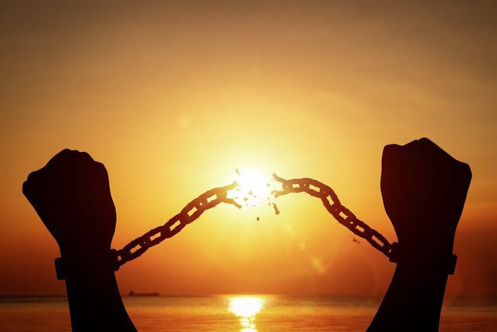 Silhouetted hands breaking a chain at sunset over calm water