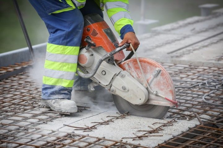 Worker using a concrete saw to cut wet pavement, with water spraying on the street