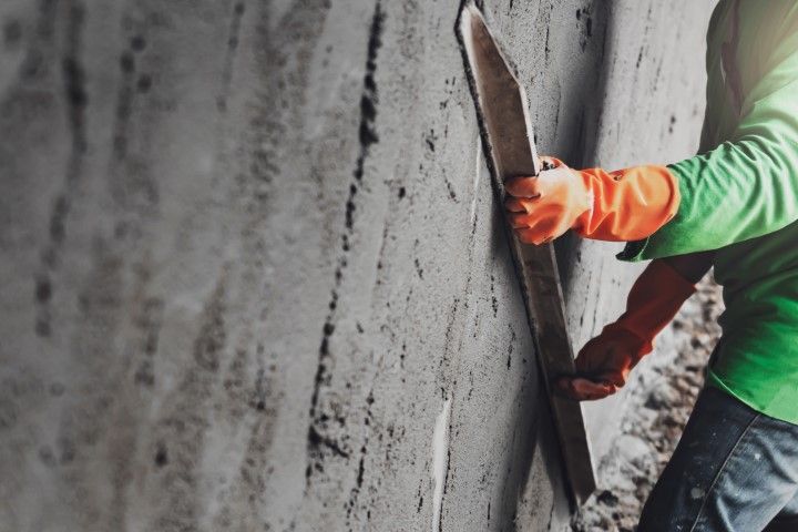 Worker in green shirt smoothing concrete wall with a trowel