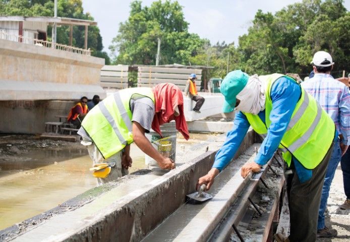 Construction workers in neon vests and helmets applying sealant to a concrete canal or bridge edge