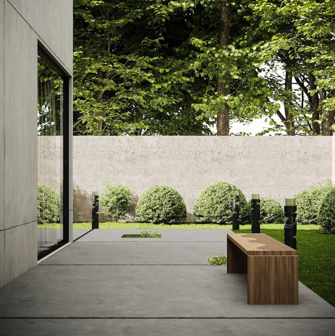 Minimalist concrete patio with a wooden bench, black posts, and shrubs beside a modern building.