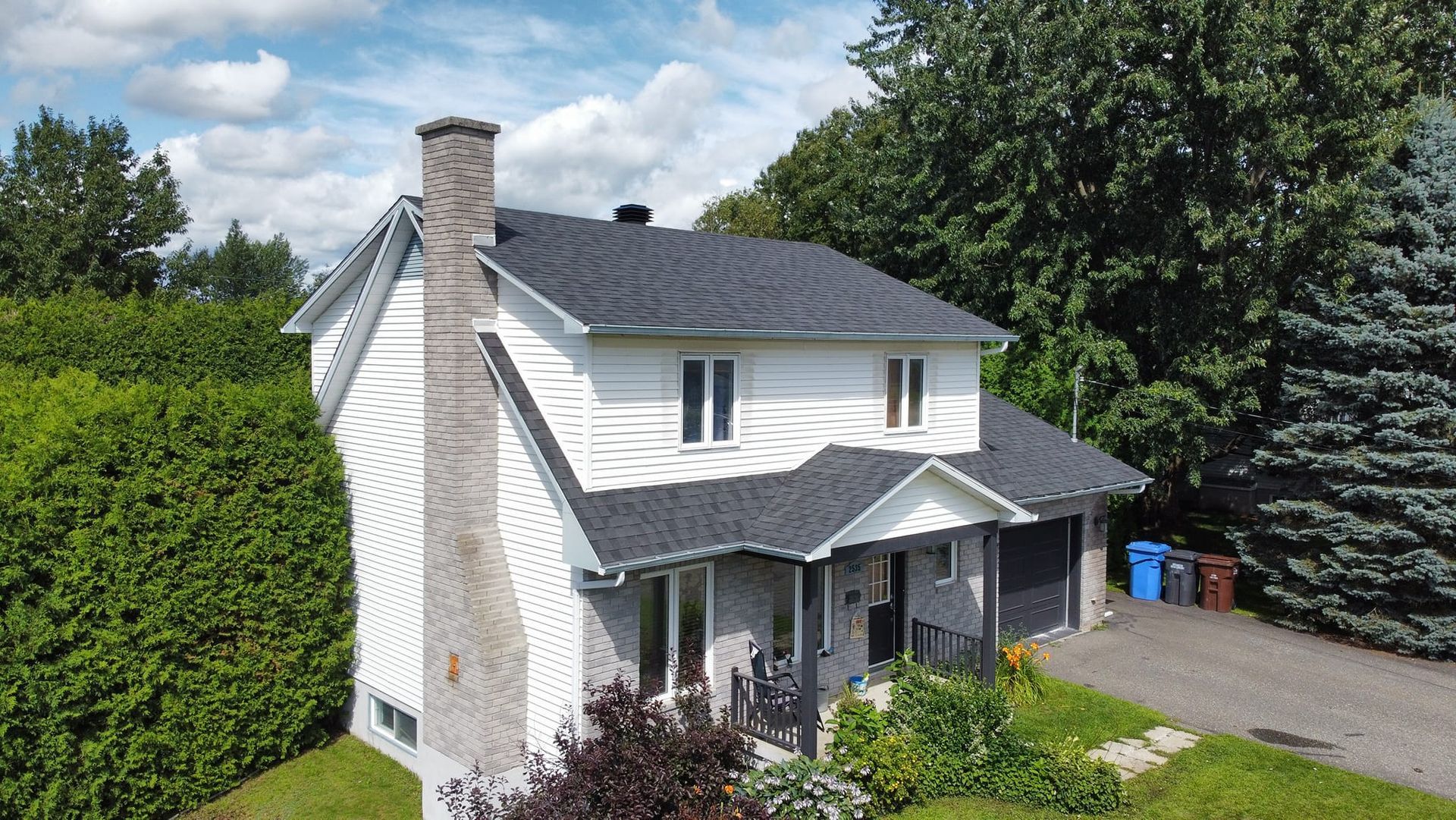 Une vue aérienne d'une maison blanche avec un toit noir entourée d'arbres.