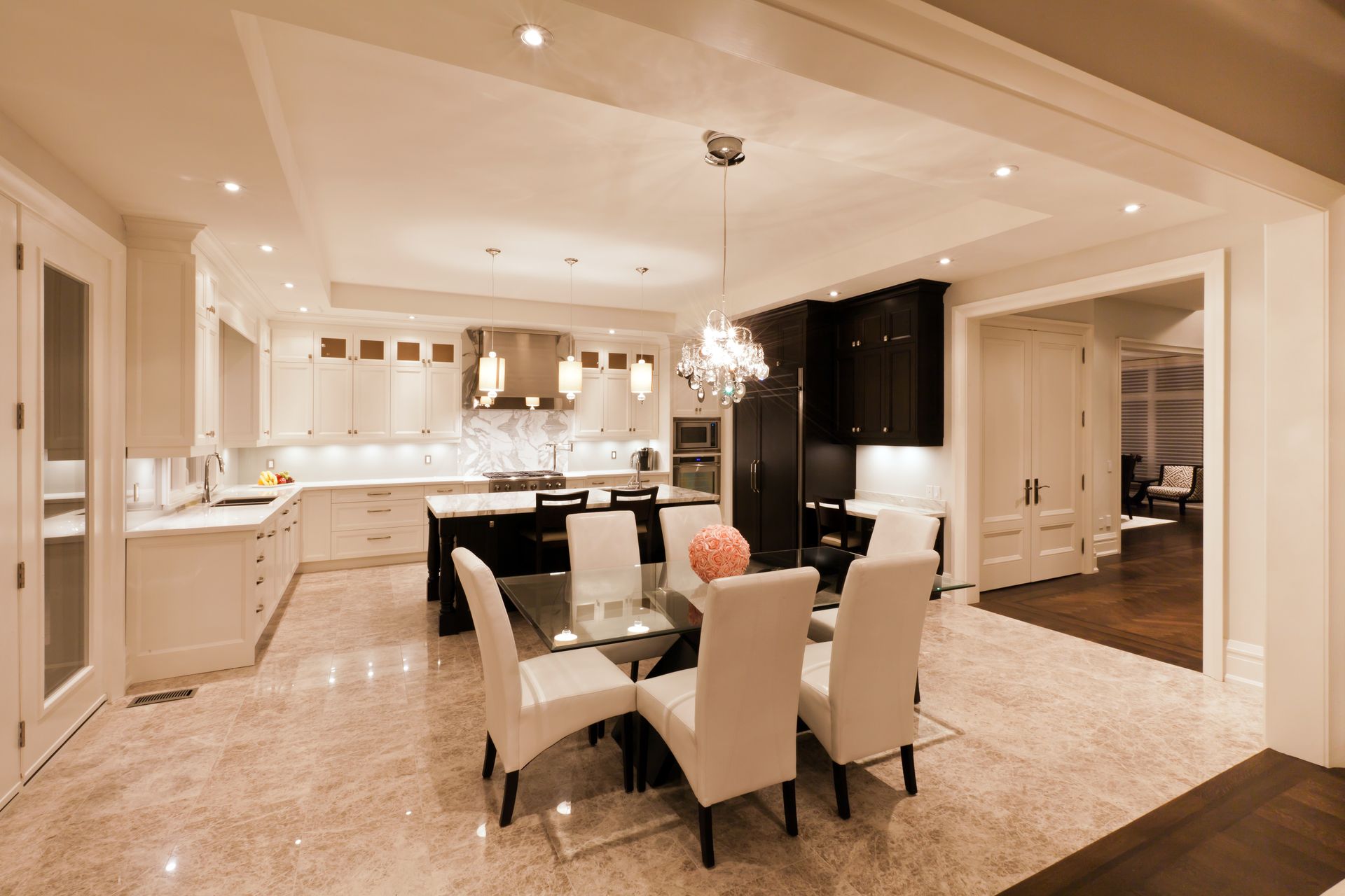 Elegant kitchen and dining area with white chairs, dark cabinets, and marble floors under warm lighting