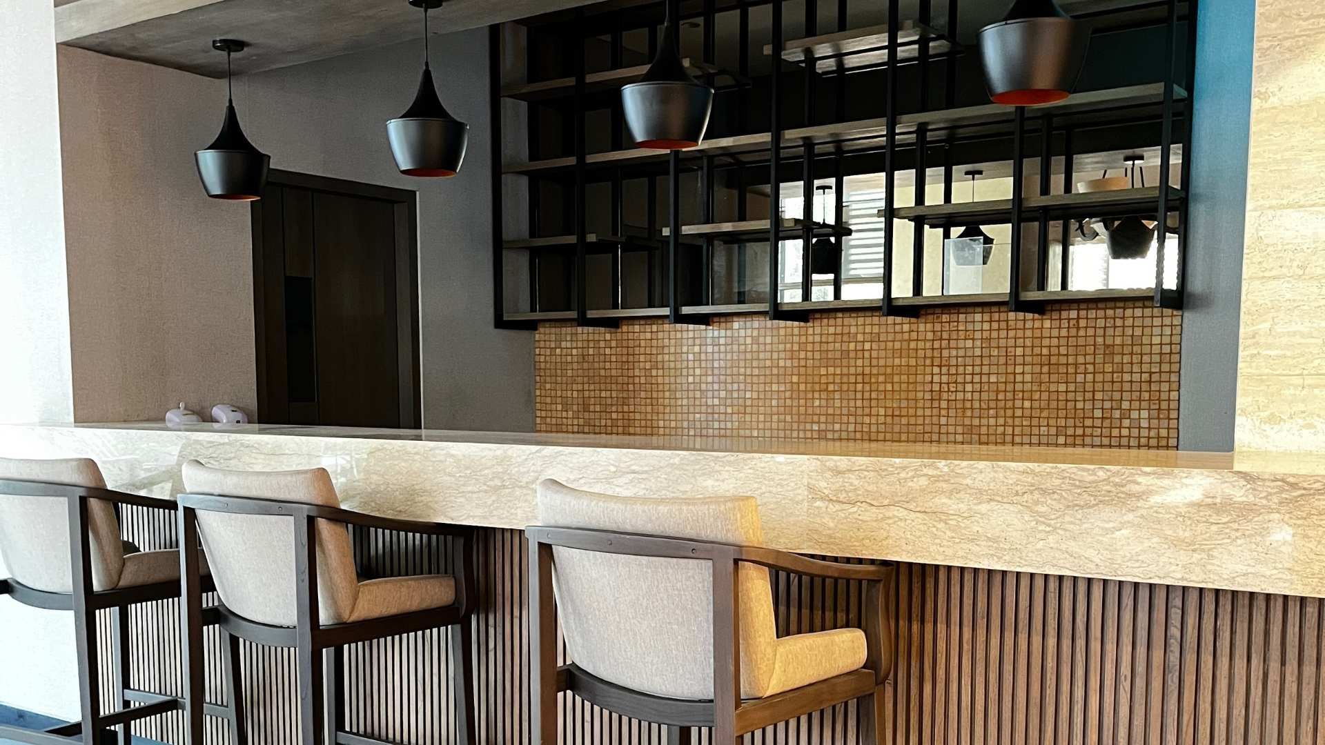 Modern café bar with wicker stools, pendant lights, and shelves behind a stone counter.