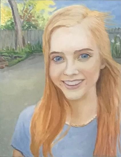 Smiling blond person in a blue shirt outdoors with a garden path and trees behind them