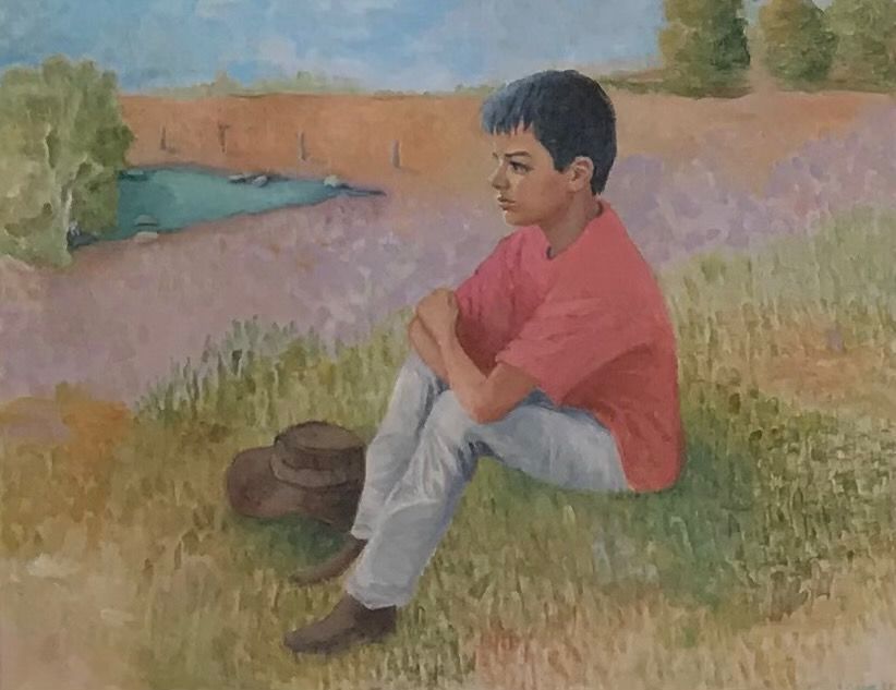 Young person in a red shirt sits on grass beside a small stream in a field of purple flowers.